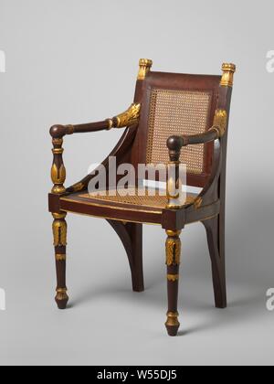 Armchair, Empire model, with cane back and seat, painted red and gilded and heightened with gold, Two armchairs (A and B) of a tropical wood (djati?), Painted red, parts gilded and heightened with gold, the back and the loose seat frame covered with reeds. Empire model with straight back, slightly arched back, widening seat with curved sides, baluster-shaped front legs and arm struts, curved, spherical-ended arms and dense cheeks with sunken fields, which are repeated below the seat in mirror image and in smaller format. Sculpted with acanthus and palmet gold motifs. Mutual differences in Stock Photo