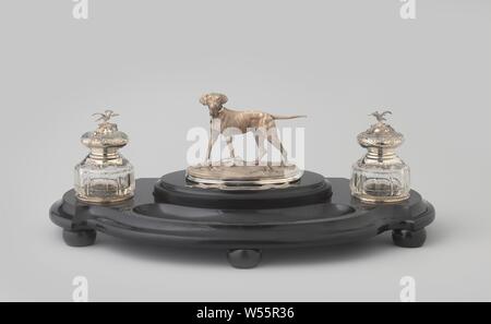 Cover Kit with standing dog, Between the two round openings are an oval and a C-shaped floor (the pen tray). A black marble lid with a straight, profiled wall fits on the oval floor. A similarly oval, low silver pedestal with sculptured plants is attached to this on a granulated foundation, with a standing dog, entirely hammered with fine grooves, with a collar with an open padlock around his neck. For this, a silver ribbon with the inscription 1836 - 1873 is mounted on the lid., Fa. As. Bonebakker en Zoon, Amsterdam, 1862, silver (metal), glass, marble (rock), grinding, h 11.5 cm × w 19.5 cm Stock Photo