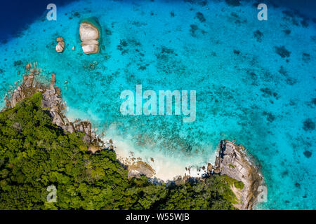 Aerial drone view of a lush tropical island with crystal clear water surrounded by coral reef Stock Photo