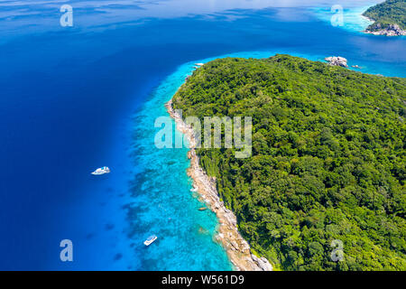 Aerial drone view of a lush tropical island with crystal clear water surrounded by coral reef Stock Photo