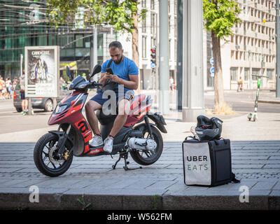 LYON, FRANCE - JULY 13, 2019: Uber Eats logo on the bag of a delivery man on his scooter, using his smartphone to wait for the next food order from a Stock Photo