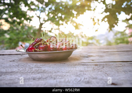 Cherry, red ripe cherries in plate and on the wooden table, background is cherry trees garden Stock Photo