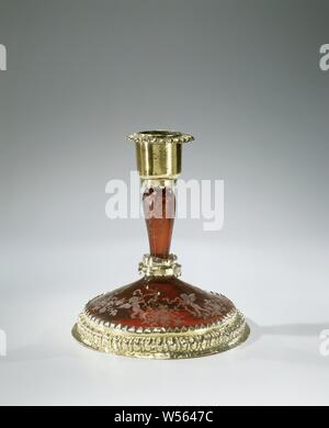 Ruby glass candlestick with gilt silver frame, conical foot, nodus under a baluster-shaped trunk, cylindrical candleholder. The edge of the foot is set in a gilt silver frame with a grunt edge and a serrated edge. The nodus and the candle holder mounted in a smooth frame with a serrated edge, the grease trap with an edge grunt. The base and stem with the wheel engraved with putti, flower festivals and flower sprays. Marked on the foot with an unknown maker's mark and the city mark of Augsburg., anonymous, c. 1700, glass, silver (metal), gilding, h 11.6 cm × d 10.5 cm Stock Photo