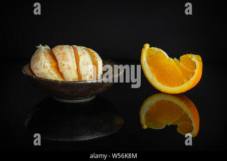 Group of one slice four pieces of fresh sweet orange in a dark ceramic bowl isolated on black glass Stock Photo