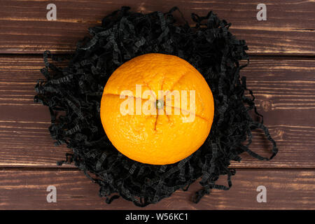 One whole fresh sweet orange on black crepe paper stripes flatlay on brown wood Stock Photo