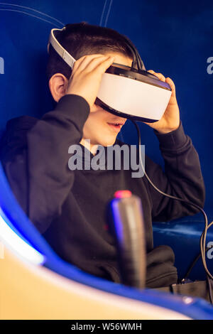 Child watching movie with VR glasses. Blue illuminated cabin with joysticks. Special effects. Technology and entertainment concept with virtual realit Stock Photo