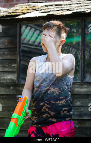 Shirtless preteen caucasian boy playing wth a water gun on a hot summer ...