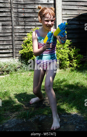 Preteen caucasian girl playing wth water guns on a hot summer's day Stock Photo