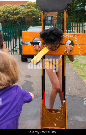 A young child throws a wet sponge at another kid held in mock stocks to raise money for charity at a school fair fête. (111) Stock Photo