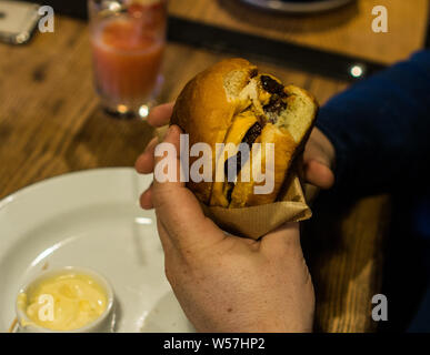 Young man's hands are holding a bitten hamburger in a fast food restaurant. Stock Photo