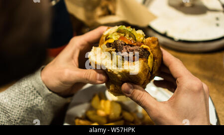 Young man's hands are holding a bitten hamburger in a fast food restaurant. Stock Photo