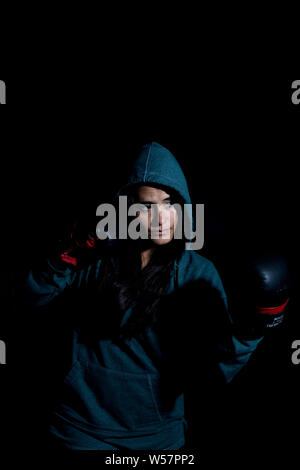 Portrait of young woman exercising boxing in the gym with red gloves on black background Stock Photo