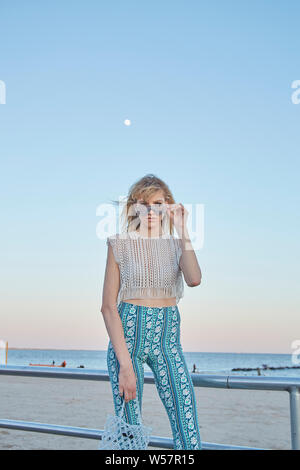 Beautiful blonde woman standing in front of beach at dusk with a full Stock Photo