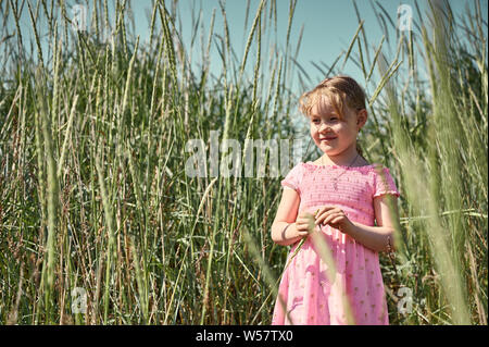 Adorable smiling little girl in pink dress standing in field on Iceland Grotta island and squinting eyes in bright light Stock Photo