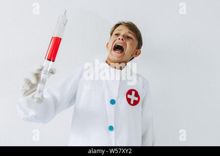 Boy impersonating himself as a scientist.  Young child playing as a mad doctor screaming with wide eyes having fun with a bloody syringe.  Concept ima Stock Photo