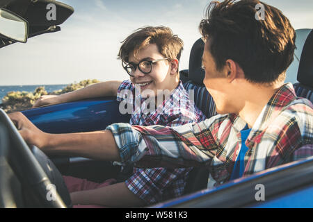 Free time, pleasure trip, concept of on the road, people. Happy friends drive a convertible car near ocean Cabriolet with teenagers. Pair of young men Stock Photo
