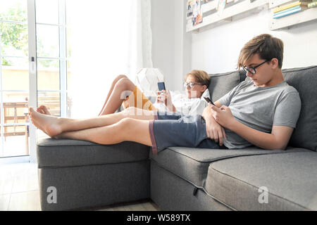 Two boys playing with smartphones lying on the sofa. Brothers using cell phone. Wireless technology allows to stay connected everywhere. Concept image Stock Photo