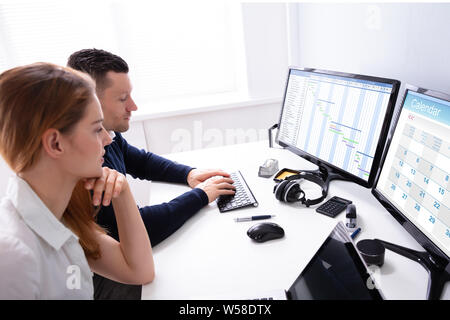 Young Businesspeople Analyzing Gantt Chart And Calendar On Computer In Office Stock Photo