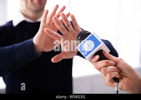 Close-up Of Female Reporter Hand's Holding Microphone While Man Refusing Interview Stock Photo