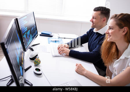 Smiling Male And Female Stock Market Broker Analyzing Graphs On Desktop At Workplace Stock Photo