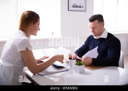 Side View Of Businesspeople Looking At Document While Interview In Office Over White Desk Stock Photo