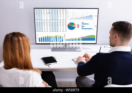 Close-up Of A Businesspeople Analyzing Graph On Computer Over The White Desk In The Office Stock Photo