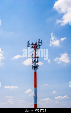 Thick red and white metal communications antenna tower against blue sky. Stock Photo