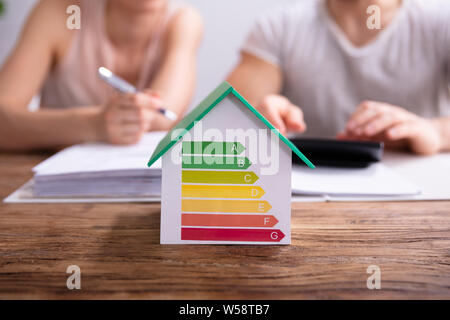 Close-up Of A House Showing Energy Efficiency Rate In Front Of Couple Using Calculator Stock Photo