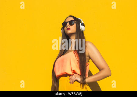 Model standing in front a yellow wall wearing sunglasses and headphones Stock Photo