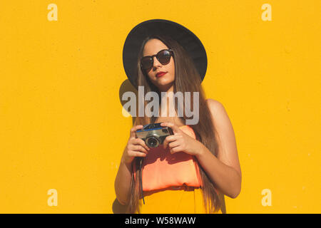 Young girl using a vintage photo camera and wearing fashionable sunglasses and a black hat Stock Photo