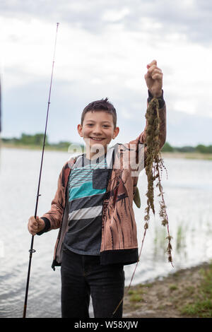 Tween boy holding up seaweed he caught fishing Stock Photo