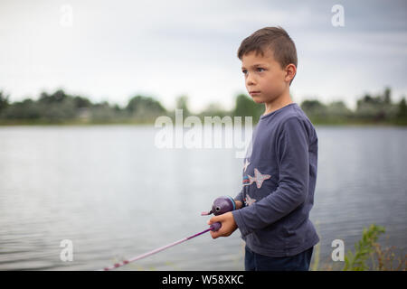 Little happy boy with a fishing rod. Cute child fishing on a lake
