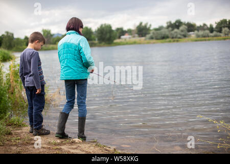 Siblings fishing in pond looking at water Stock Photo