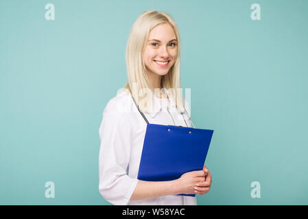 Portrait of an attractive young female doctor in white coat on blue background Stock Photo