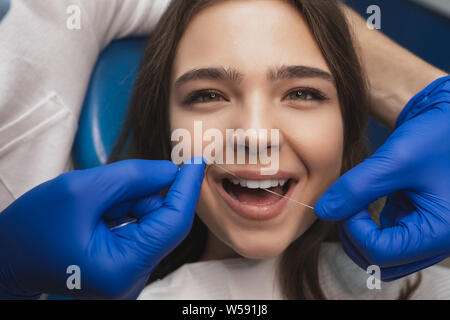 dentist in blue medical gloves cleaning woman patient's teeth using dental floss in clinic Stock Photo