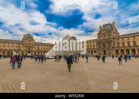 Panoramic view of the famous Louvre Museum in Paris. In the courtyard a male visitor is walking towards the iconic glass pyramid, one of Louvre's... Stock Photo