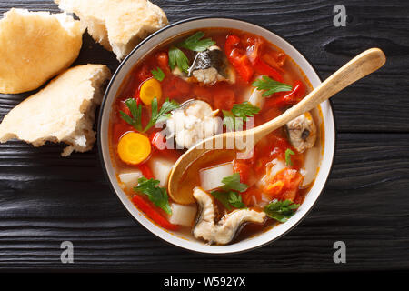 Eel soup with tomatoes, potatoes, carrots, onions, peppers and herbs closeup in a bowl on the table. horizontal top view from above Stock Photo