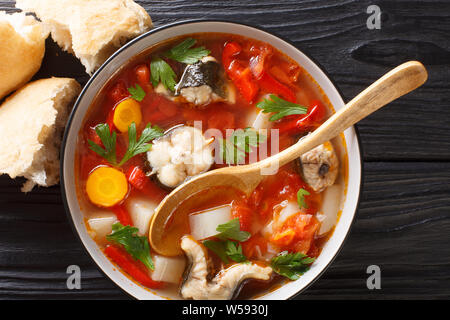Spicy fish soup with eel, tomatoes and other vegetables close-up in a bowl served with bread on the table. horizontal top view from above Stock Photo