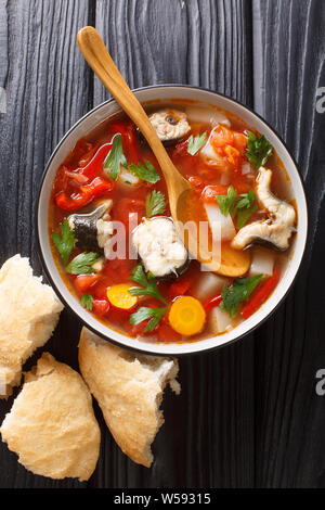 Eel soup with tomatoes, potatoes, carrots, onions, peppers and herbs closeup in a bowl on the table. Vertical top view from above Stock Photo
