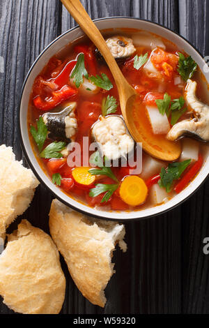 Spicy fish soup with eel, tomatoes and other vegetables close-up in a bowl served with bread on the table. Vertical top view from above Stock Photo