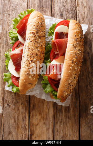 Fresh prosciutto ham sandwiches, mozzarella cheese and vegetables close-up on the table. Vertical top view from above Stock Photo