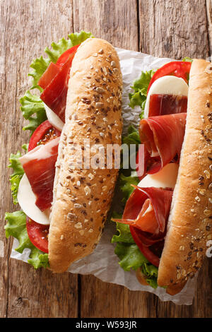 Delicious Italian sandwiches with prosciutto ham, mozzarella cheese and vegetables close-up on the table. Vertical top view from above Stock Photo