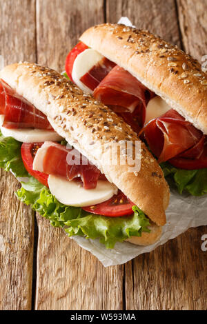 Fresh prosciutto ham sandwiches, mozzarella cheese and vegetables close-up on the table. vertical Stock Photo