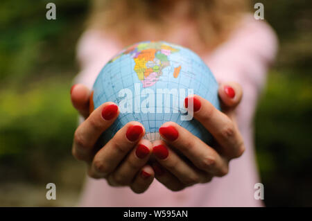 The girl in a pink sweater with red manicure holds a small globe with geografical names in Ukrainian cyrillic letters on it. African continent and Stock Photo
