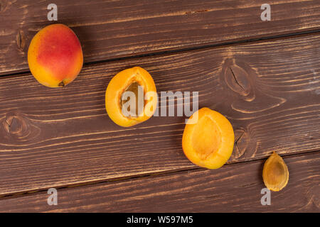 Group of one whole two halves one piece of fresh orange apricot with an apricot stone flatlay on brown wood Stock Photo
