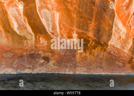 Sandstone cliff canyon wall  in colorful shades of red, orange, and yellow above a clear stream - Oak Creek, Sedona, Arizona Stock Photo