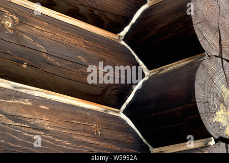Corner connection of wooden log house. Timber house wall from wood logs. Dark brown burnt texture. Close-up top angle view. Wood annual rings. Green b Stock Photo