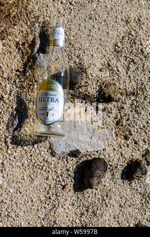 Empty glass bottle with label discarded on ground in desert. Stock Photo