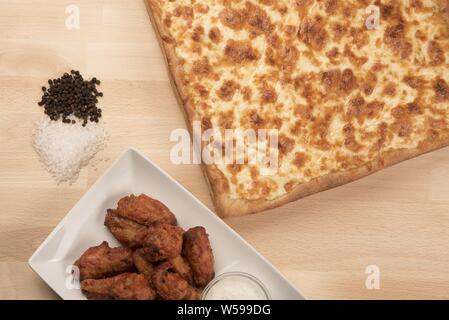 Overhead shot of chicken wings in a bowl with a square-shaped cheese pizza Stock Photo
