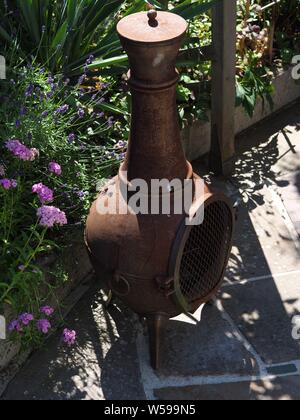 Old metal outdoor oven on a natural stone terrace in front of a flowerbed Stock Photo